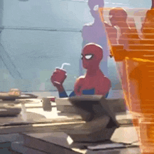 a spider-man is sitting at a desk drinking a drink from a cup .
