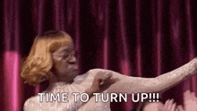 a woman is dancing on a stage with the words `` time to turn up '' written on the screen .