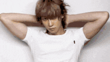 a man with his hands behind his head is wearing a white t-shirt