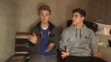 two boys are sitting next to each other in a room and one of them is wearing a blue shirt