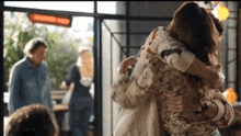 two women are hugging each other in a restaurant while a man stands in the background .