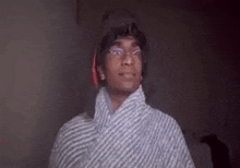 a man wearing glasses and a striped shirt is standing in a dark room .