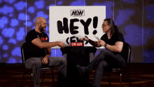 two men sit in front of a sign that says hey on air