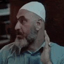 a man with a beard is wearing a white hat and adjusting his ear .
