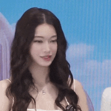 a woman with long brown hair is wearing a white tank top and necklace .