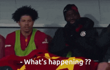a man sitting next to another man with the words what 's happening written on the bottom
