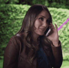 a woman in a brown leather jacket is talking on her cell phone