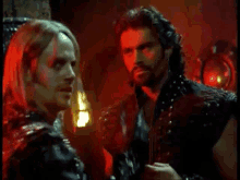 two men are standing next to each other in a dark room with red lights behind them .