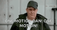 a man in a hat is standing in front of a building and says `` one motion dan ! one motion ! '' .