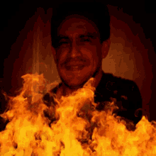 a man is smiling in front of a wall of flames