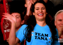 a woman wearing a blue shirt that says team tana is smiling