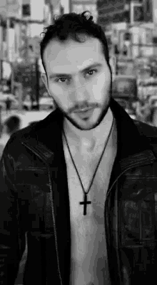 a man wearing a leather jacket and a cross necklace is standing in a black and white photo .
