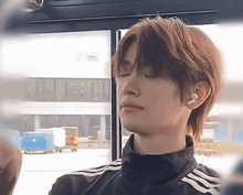a young man is sitting in a bus with his eyes closed and wearing ear buds .