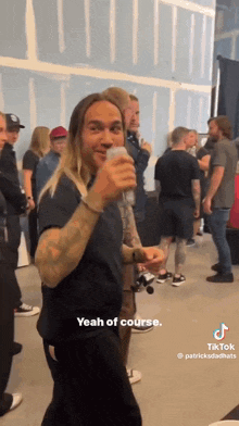 a man with long blonde hair is drinking from a can while standing in a crowd of people .