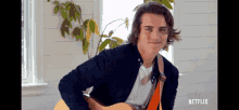 a man playing a guitar in front of a window with netflix written on the bottom