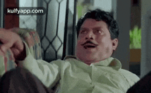 a man with a mustache is sitting on a couch with his legs crossed .