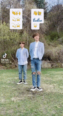 two young men standing in a grassy field with trees in the background ..