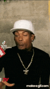 a man wearing a hat and a necklace is making a face .