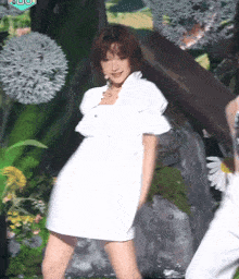 a woman in a white dress is dancing on a stage with flowers in the background