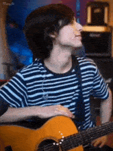 a young man in a blue and white striped shirt is playing an acoustic guitar .