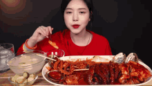 a woman in a red shirt is eating a large plate of food with chopsticks