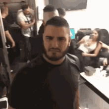 a man with a beard wearing a black shirt is standing in a crowded room .