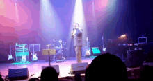 a man singing into a microphone on a stage with guitars in the background