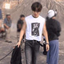 a man wearing a white t-shirt that says pleasures is walking