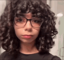a girl with curly hair and glasses is taking a selfie in a bathroom .