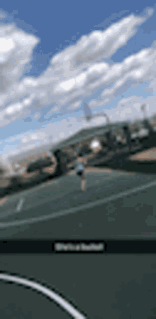 a blurry picture of a basketball court with a blue sky and clouds in the background .