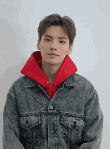 a young man wearing a grey denim jacket and a red hoodie .