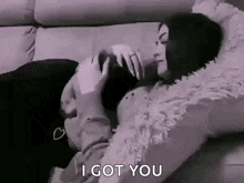 a man and woman are laying on a couch and the woman is kissing the man 's forehead .