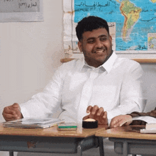 a man in a white shirt sits at a desk in front of a map