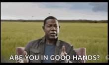 a man is sitting in a chair in front of a field and asking are you in good hands ?
