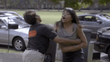 a man is holding a woman in his arms while they are fighting in front of a parking lot .