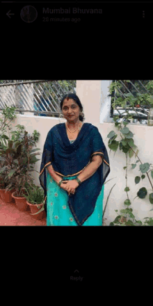 a woman in a blue dress is standing in front of some potted plants