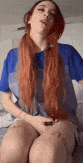 a woman with long red hair is sitting on a table with her legs crossed and a kiss written on her leg .