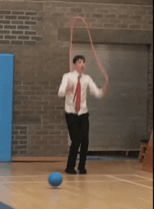 a man in a white shirt and red tie is kicking a blue ball on a basketball court