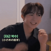 a young man in a black shirt is smiling in a room with chinese writing on the bottom