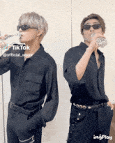 a man drinking a bottle of water next to another man with sunglasses