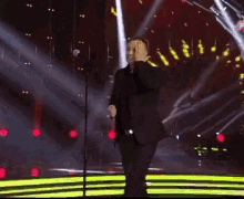a man in a black suit is singing into a microphone on stage