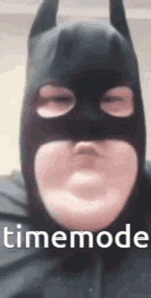 a close up of a person wearing a batman mask with the words timemode on the bottom .