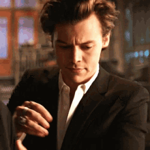 a man in a suit and white shirt is smoking a cigarette while wearing a ring on his finger .