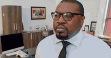 a man wearing glasses and a tie sits at a desk in front of a computer