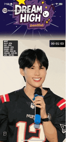 a man in a patriots jersey is holding a microphone and smiling