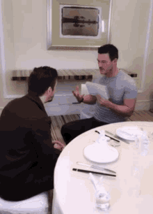 two men sitting at a table with plates and chopsticks