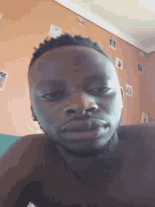 a shirtless man is taking a selfie in front of an orange wall with pictures on it .