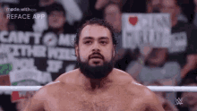 a man with a beard is standing in a wrestling ring with a crowd in the background .