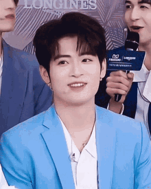 a young man in a blue suit is holding a microphone and smiling