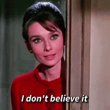 a woman in a red sweater is peeking out of a door and saying `` i don 't believe it ''